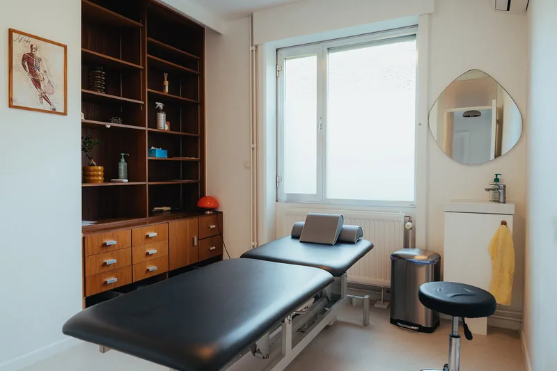 Vue d'ensemble d'une salle de soin avec table de massage, meuble en bois et lavabo