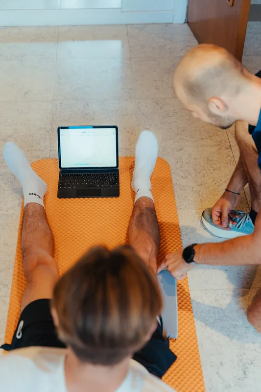 Vue plongeante sur un patient allongé jambes tendues, tablette affichant un graphique de mesure